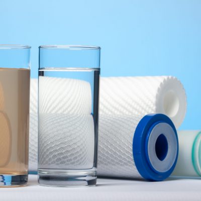 Glasses of dirty and clear water and filter cartridges to domestic water treatment systems at bright blue background. Concept of water treatment.